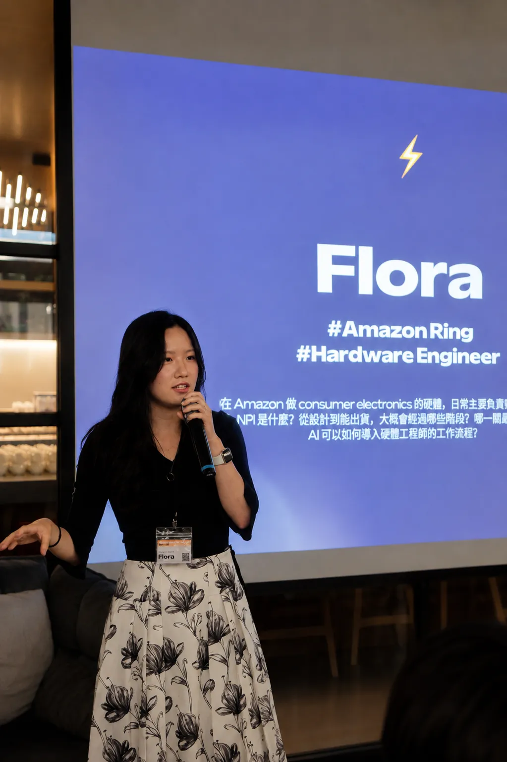 Flora Liu speaking on stage at Techie Talk 2026, in front of a slide introducing her work as a hardware engineer.